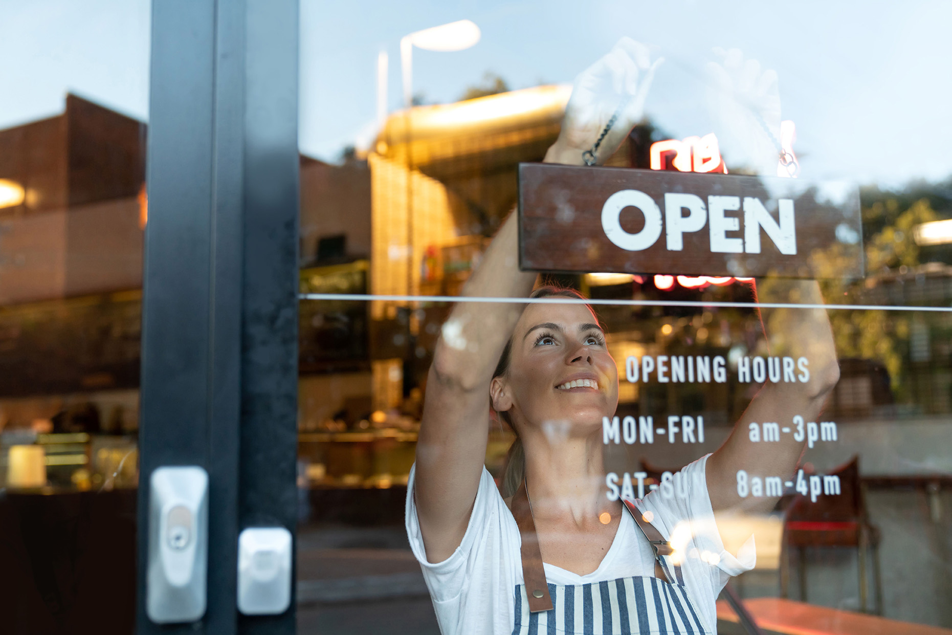 A woman in an apron is looking through the window of her business.