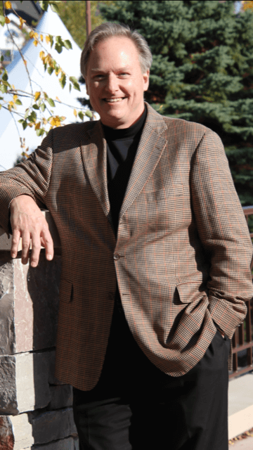 A man in a brown suit leaning on a wall.